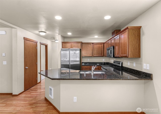 1422 Lincoln St, Bellingham, WA 98229 - kitchen featuring appliances with stainless steel finishes, a peninsula, dark stone counters, light wood finished floors, and brown cabinets