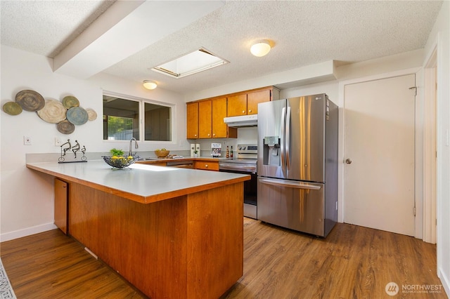 17114 SE 130th Ave, Renton, WA 98058 - kitchen with appliances with stainless steel finishes, under cabinet range hood, a peninsula, brown cabinetry, and wood finished floors