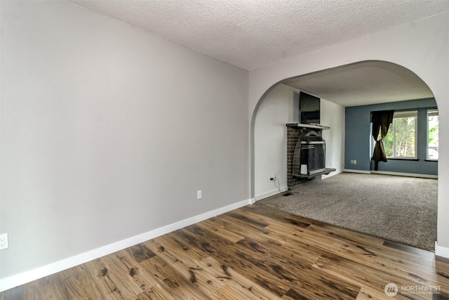 416 142nd Street Ct S, Tacoma, WA 98444 - unfurnished living room with arched walkways, a brick fireplace, wood finished floors, and a textured ceiling