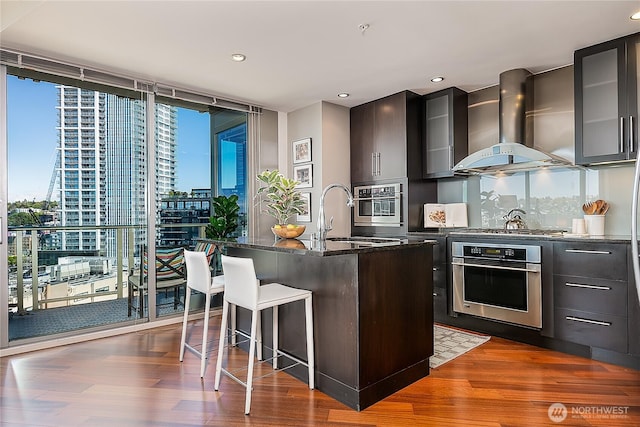 2121 Terry Ave Unit 1402, Seattle, WA 98121 - kitchen with appliances with stainless steel finishes, wall chimney range hood, dark wood-type flooring, a kitchen breakfast bar, and a wall of windows