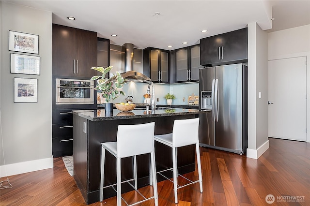 2121 Terry Ave Unit 1402, Seattle, WA 98121 - kitchen with stainless steel appliances, wall chimney range hood, an island with sink, glass insert cabinets, and dark wood-style flooring