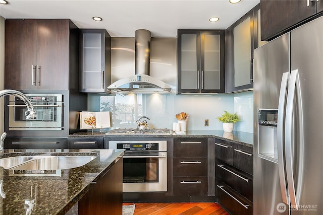 2121 Terry Ave Unit 1402, Seattle, WA 98121 - kitchen with stainless steel appliances, wall chimney range hood, glass insert cabinets, wood finished floors, and dark brown cabinetry
