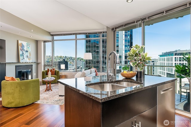 2121 Terry Ave Unit 1402, Seattle, WA 98121 - kitchen with wood finished floors, dishwasher, a glass covered fireplace, a kitchen island with sink, and dark stone countertops