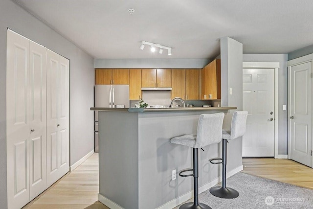 7711 NE 175th St Unit E110, Kenmore, WA 98028 - kitchen with freestanding refrigerator, a breakfast bar area, brown cabinets, a peninsula, and light wood-style flooring