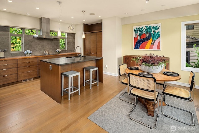 5115 NE Latimer Pl, Seattle, WA 98105 - kitchen with island exhaust hood, brown cabinets, a kitchen breakfast bar, light wood-style floors, and recessed lighting