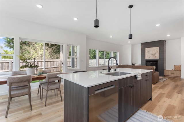 4710 Sagebrush Ln, Blaine, WA 98230 - kitchen with stainless steel dishwasher, light wood-style flooring, light countertops, a large fireplace, and a kitchen island with sink