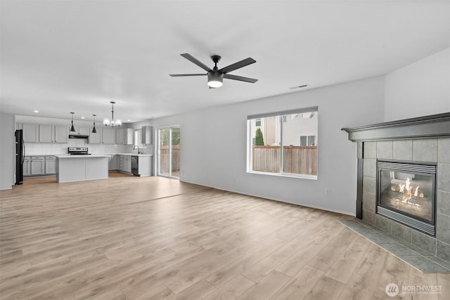 14933 Terra View St SE, Yelm, WA 98597 - unfurnished living room with a chandelier, a tiled fireplace, a ceiling fan, light wood-style flooring, and recessed lighting