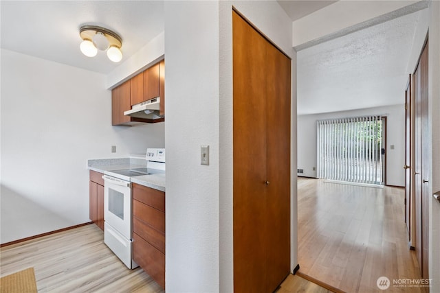 18910 Bothell Everett Hwy Unit K3, Bothell, WA 98012 - kitchen featuring white electric stove, under cabinet range hood, light wood finished floors, brown cabinets, and light countertops