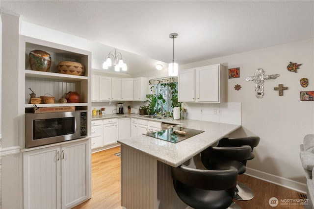 7829 197th Ave E, Bonney Lake, WA 98391 - kitchen featuring stainless steel microwave, black electric stovetop, a peninsula, a kitchen bar, and light wood finished floors