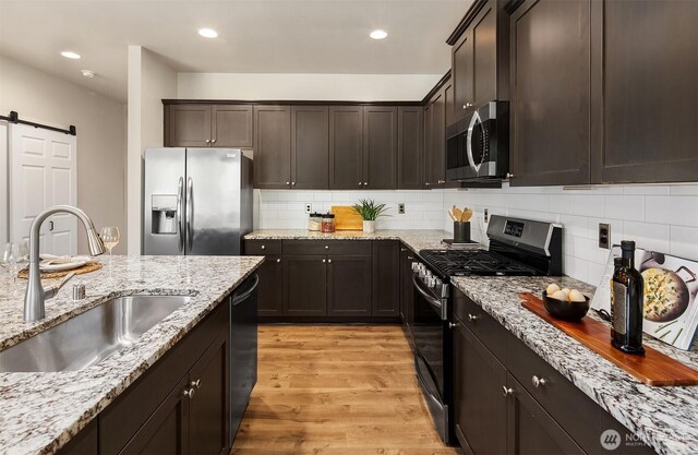 12611 37th Pl NE, Lake Stevens, WA 98258 - kitchen featuring appliances with stainless steel finishes, a barn door, light wood-style floors, tasteful backsplash, and dark brown cabinetry