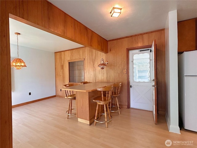 304 Columbia Ave, Coulee Dam, WA 99116 - kitchen with freestanding refrigerator, wood walls, light wood-style floors, a breakfast bar, and a peninsula