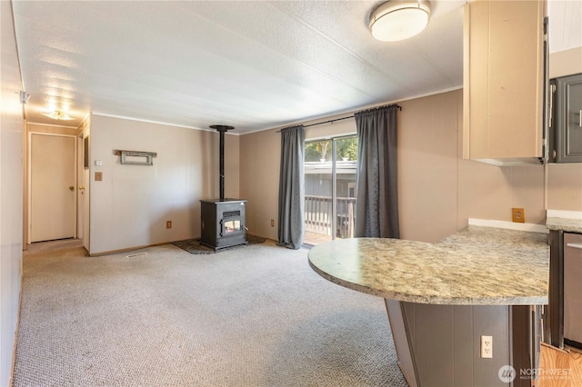 7138 Englewood Dr SE Unit 32, Olympia, WA 98513 - kitchen featuring a wood stove, light countertops, a peninsula, light colored carpet, and crown molding