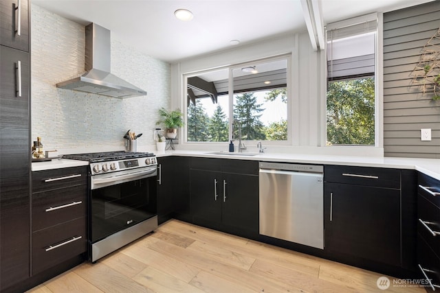 1432 Weathervane Dr, Fircrest, WA 98466 - kitchen featuring appliances with stainless steel finishes, wall chimney exhaust hood, dark cabinetry, and light wood-style flooring
