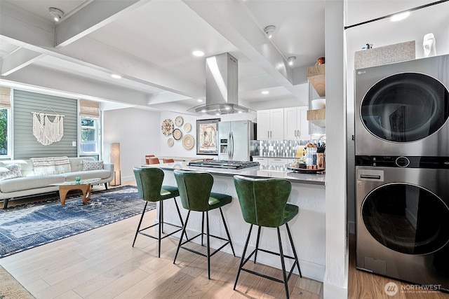 1432 Weathervane Dr, Fircrest, WA 98466 - kitchen with island exhaust hood, stacked washer and clothes dryer, stainless steel appliances, a kitchen breakfast bar, and beamed ceiling