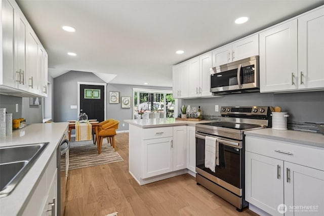 14427 156th Ave SE, Renton, WA 98059 - kitchen with stainless steel appliances, a peninsula, light wood finished floors, white cabinets, and lofted ceiling