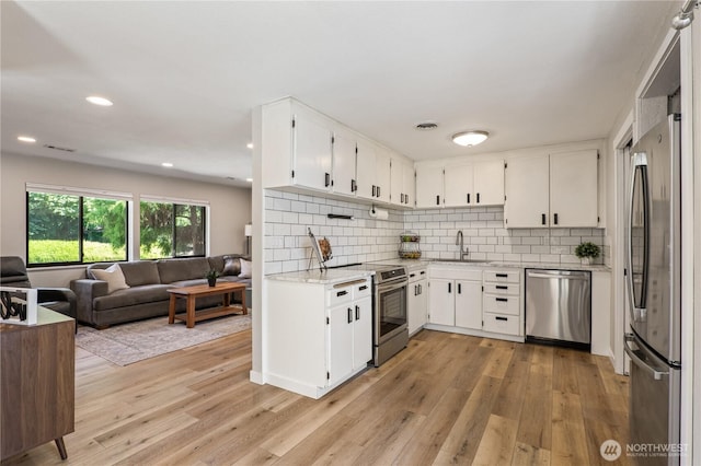 4502 223rd St SW, Mountlake Terrace, WA 98043 - kitchen featuring stainless steel appliances, open floor plan, light wood finished floors, decorative backsplash, and white cabinets