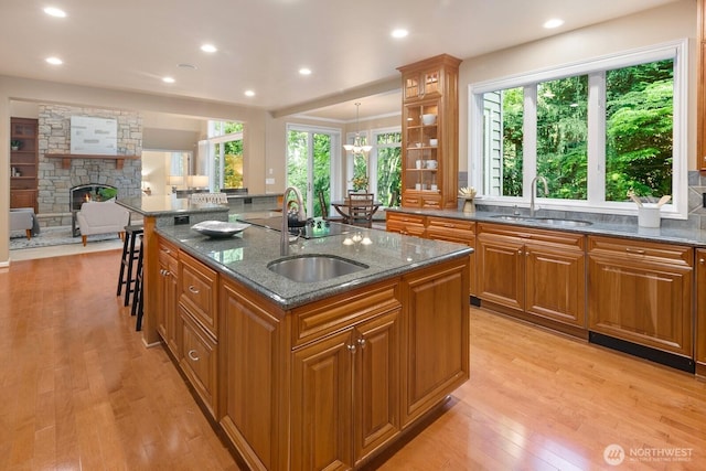 13695 NE 32nd Pl, Bellevue, WA 98005 - kitchen featuring brown cabinetry, an island with sink, a fireplace, light wood-type flooring, and dark stone counters
