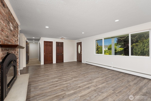 10414 43rd Street Ct E, Edgewood, WA 98372 - unfurnished living room with baseboard heating, wood finished floors, a textured ceiling, recessed lighting, and a fireplace