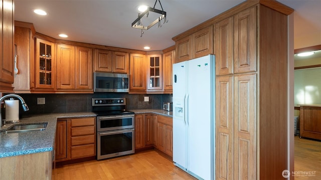 755 Ferry Rd, Lopez Island, WA 98261 - kitchen with appliances with stainless steel finishes, brown cabinetry, tasteful backsplash, light wood-style floors, and glass insert cabinets