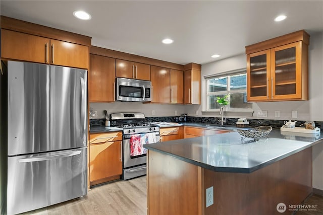 923 N 85th St Unit A, Seattle, WA 98103 - kitchen featuring appliances with stainless steel finishes, a peninsula, light wood-type flooring, dark countertops, and glass insert cabinets