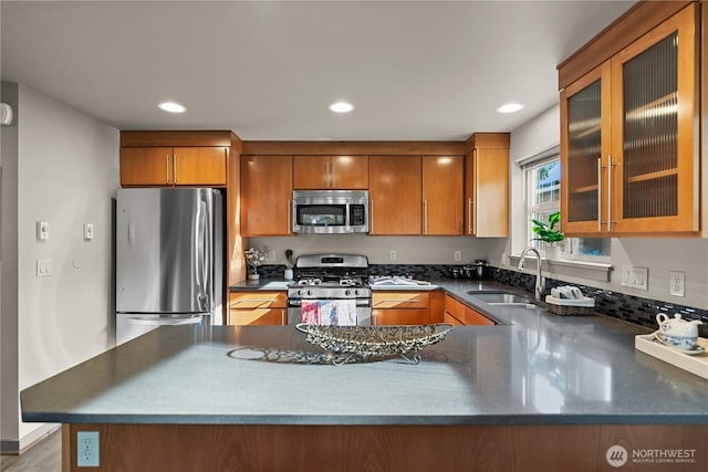 923 N 85th St Unit A, Seattle, WA 98103 - kitchen featuring appliances with stainless steel finishes, brown cabinets, a peninsula, dark countertops, and glass insert cabinets