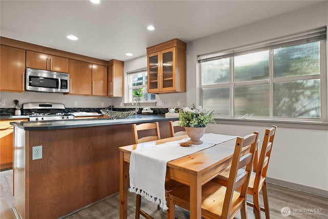 923 N 85th St Unit A, Seattle, WA 98103 - kitchen featuring appliances with stainless steel finishes, light wood-type flooring, dark countertops, brown cabinetry, and glass insert cabinets
