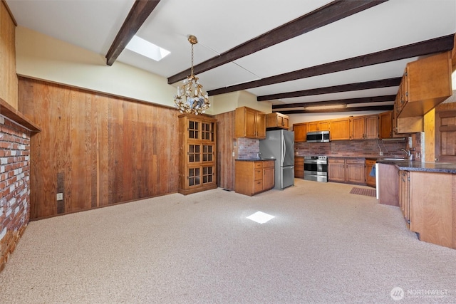 714 Canterbury Rd NW, Soap Lake, WA 98851 - kitchen with stainless steel appliances, beamed ceiling, brown cabinetry, decorative backsplash, and carpet flooring