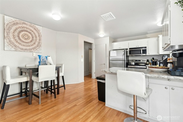 10421 19th Ave SE, Everett, WA 98208 - kitchen featuring stainless steel appliances, a peninsula, white cabinetry, light wood-style floors, and a kitchen bar