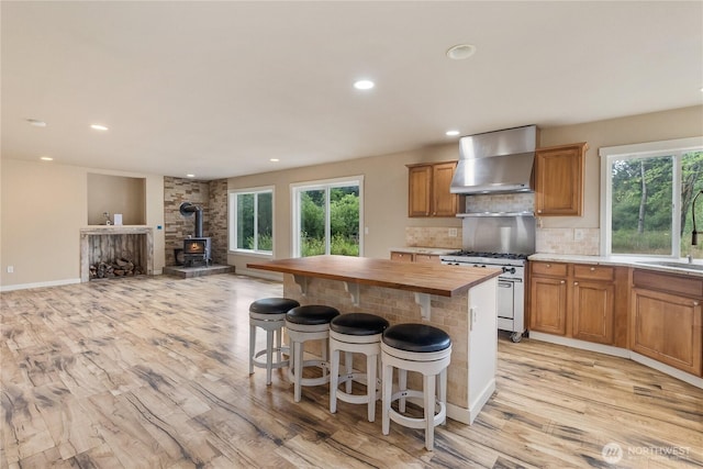 932 Tipsoo Loop N, Rainier, WA 98576 - kitchen featuring wall chimney range hood, stainless steel stove, butcher block counters, a wood stove, and light wood finished floors