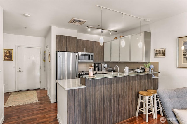3104 Western Ave Unit 610, Seattle, WA 98121 - kitchen with appliances with stainless steel finishes, a peninsula, dark wood finished floors, a breakfast bar area, and rail lighting