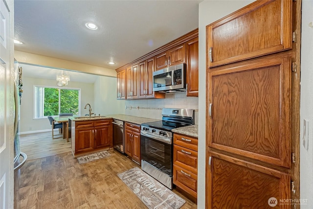 4164 Factoria Blvd SE Unit B11, Bellevue, WA 98006 - kitchen with stainless steel appliances, a peninsula, light wood-style flooring, a chandelier, and brown cabinetry