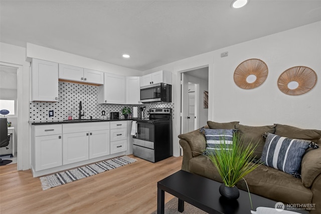 1027 E 47th St, Tacoma, WA 98404 - kitchen featuring appliances with stainless steel finishes, open floor plan, dark countertops, light wood-type flooring, and backsplash