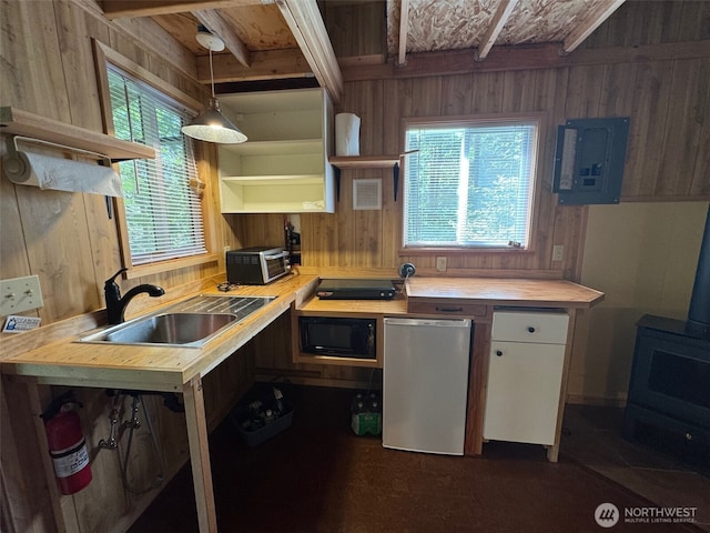 7379 Hideaway Ln, Anacortes, WA 98221 - kitchen with open shelves, wooden walls, a wood stove, electric panel, and white cabinets