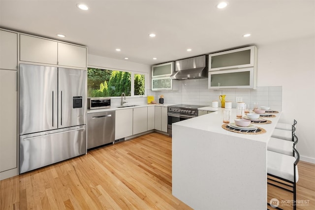 2434 64th Ave SE, Mercer Island, WA 98040 - kitchen featuring stainless steel appliances, a peninsula, wall chimney exhaust hood, light wood finished floors, and tasteful backsplash
