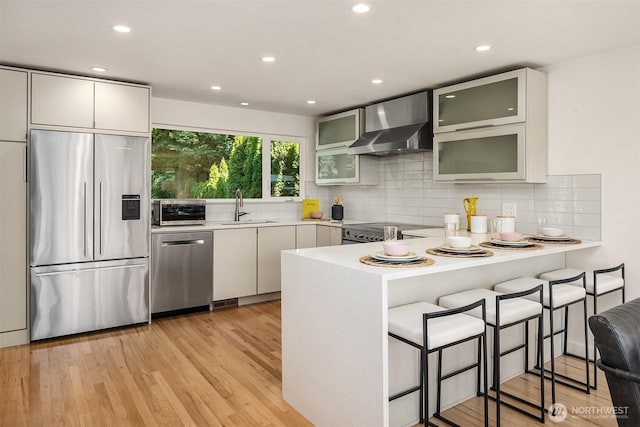 2434 64th Ave SE, Mercer Island, WA 98040 - kitchen featuring stainless steel appliances, wall chimney exhaust hood, a peninsula, light wood-type flooring, and light countertops