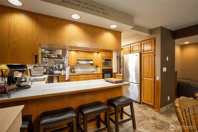 1130 Central Dr, Coulee Dam, WA 99116 - kitchen with black appliances, under cabinet range hood, a peninsula, light countertops, and a breakfast bar
