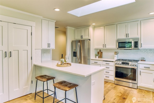4957 Lewis Ave, Bellingham, WA 98229 - kitchen featuring appliances with stainless steel finishes, a skylight, light countertops, a breakfast bar, and white cabinetry