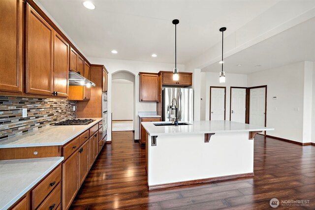 22820 41st Dr SE, Bothell, WA 98021 - kitchen featuring appliances with stainless steel finishes, brown cabinets, dark wood finished floors, arched walkways, and a kitchen island with sink