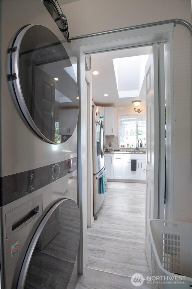 118 Ocean Lake Way NE, Ocean Shores, WA 98569 - laundry area featuring stacked washing machine and dryer, light wood-style floors, and a skylight