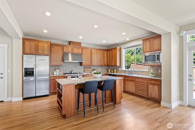 2648 116th Ave NE, Bellevue, WA 98004 - kitchen with built in appliances, under cabinet range hood, light wood-style flooring, an island with sink, and decorative backsplash