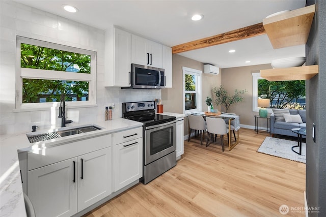 3130 SW 97th St, Seattle, WA 98126 - kitchen featuring appliances with stainless steel finishes, a wall mounted air conditioner, white cabinetry, backsplash, and light wood-type flooring