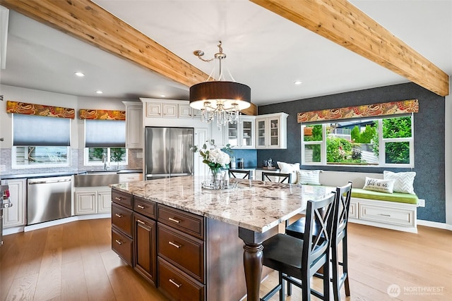 3406 SW Manning St, Seattle, WA 98126 - kitchen featuring stainless steel appliances, beamed ceiling, light wood-style flooring, a chandelier, and a kitchen breakfast bar