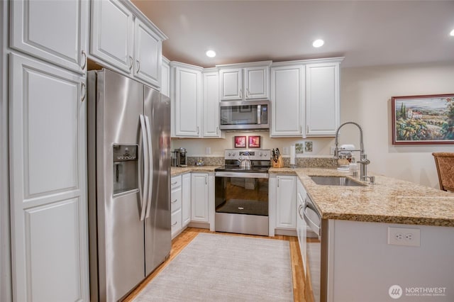 789 Island Cir SE, Ocean Shores, WA 98569 - kitchen featuring stainless steel appliances, a peninsula, white cabinets, light wood-style floors, and light stone countertops