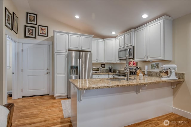789 Island Cir SE, Ocean Shores, WA 98569 - kitchen with stainless steel appliances, a peninsula, light stone counters, light wood-type flooring, and recessed lighting
