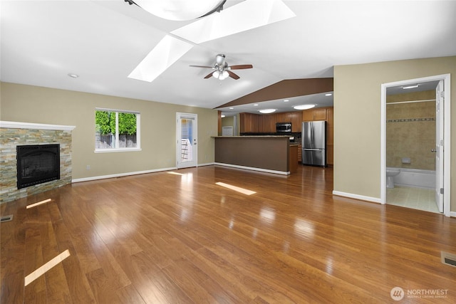 22526 87th Pl W, Edmonds, WA 98026 - unfurnished living room featuring a skylight, wood finished floors, a fireplace, vaulted ceiling, and ceiling fan