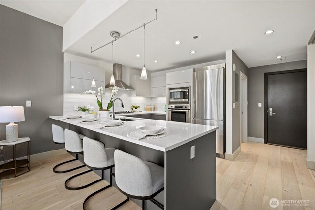 737 Olive Way Unit 1903, Seattle, WA 98101 - kitchen featuring appliances with stainless steel finishes, wall chimney exhaust hood, a peninsula, light countertops, and a kitchen breakfast bar