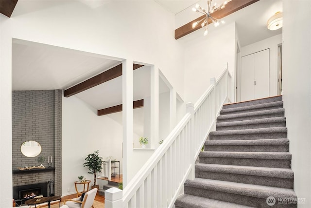 6687 NE Bayview Blvd, Bainbridge Island, WA 98110 - staircase with beam ceiling, high vaulted ceiling, a brick fireplace, a chandelier, and wood finished floors