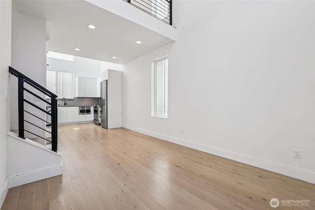 805 Taylor Ave N Unit D, Seattle, WA 98109 - unfurnished living room with stairway, light wood-style flooring, recessed lighting, a towering ceiling, and plenty of natural light