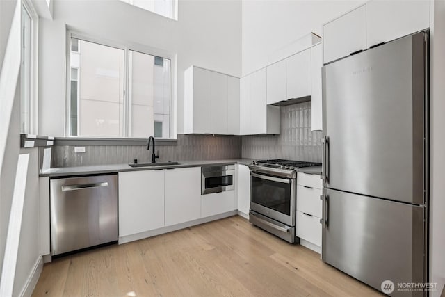 805 Taylor Ave N Unit D, Seattle, WA 98109 - kitchen featuring stainless steel appliances, white cabinets, tasteful backsplash, and a high ceiling