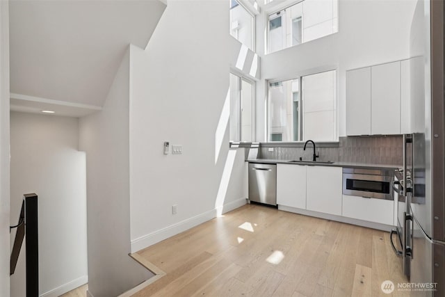 805 Taylor Ave N Unit D, Seattle, WA 98109 - kitchen featuring appliances with stainless steel finishes, white cabinetry, light wood-type flooring, modern cabinets, and decorative backsplash